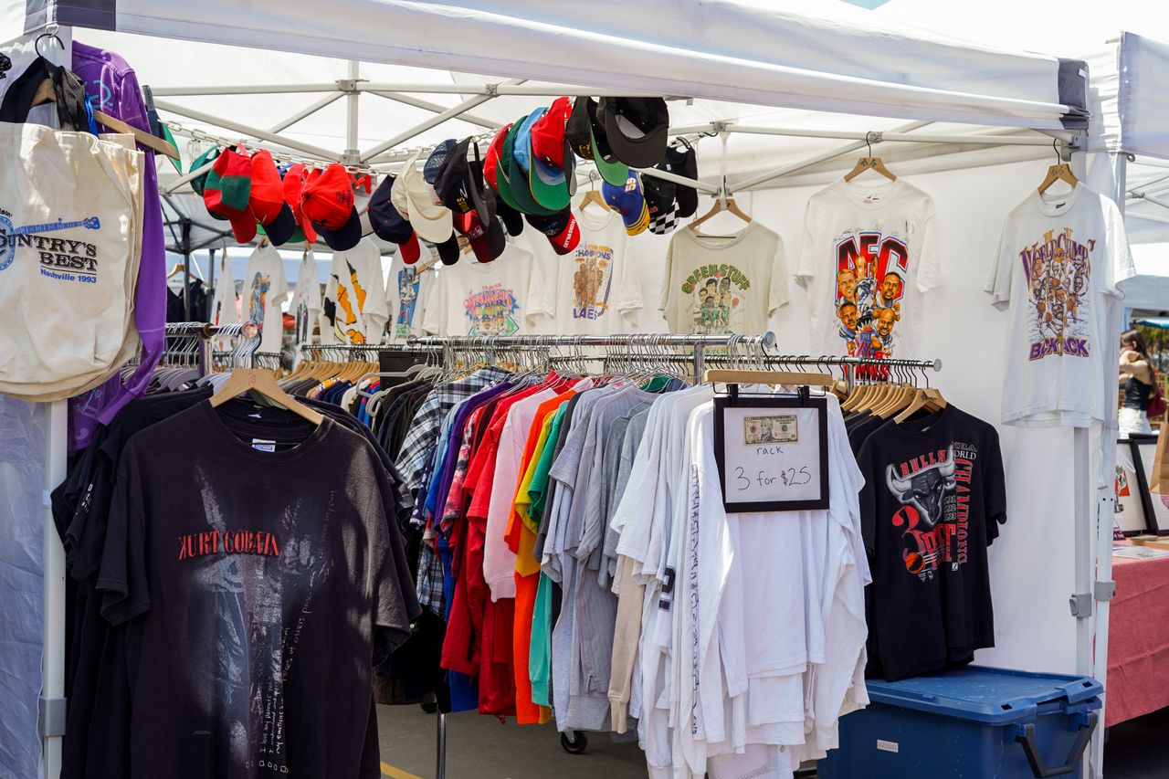 A vibrant street market stall featuring a variety of colorful t-shirts and caps under a tent.