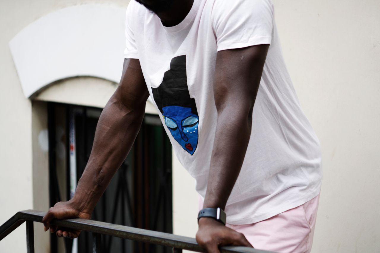 Man wearing a white t-shirt with a colorful artistic design, leaning on a handrail.
