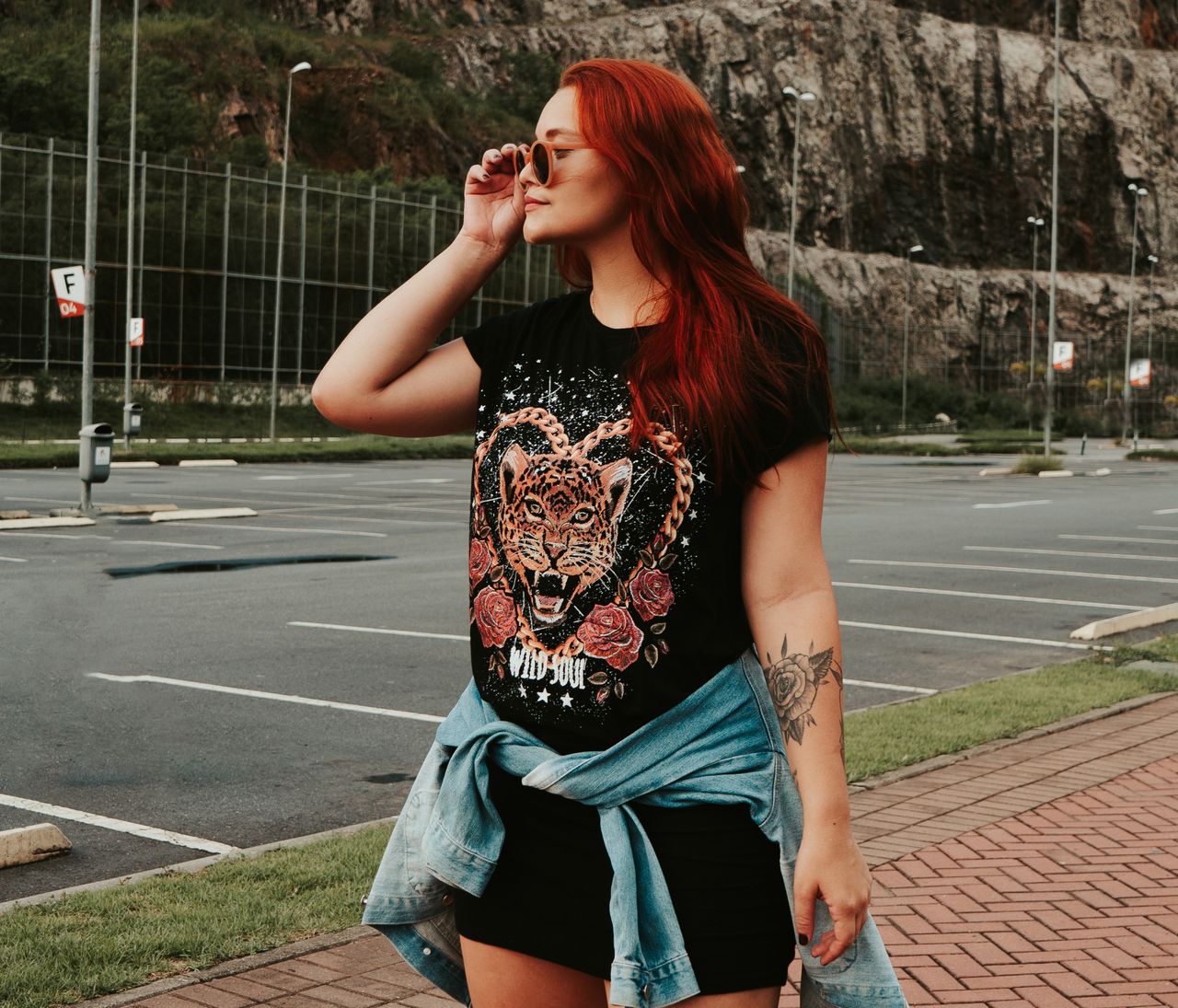 Fashionable woman with red hair wearing sunglasses and printed t-shirt outdoors.